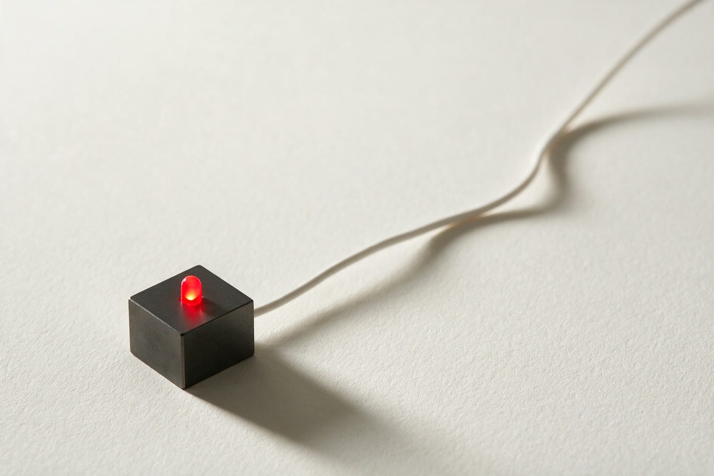 Bloc mat anthracite à diode vermillon, câble fin sur papier clair.